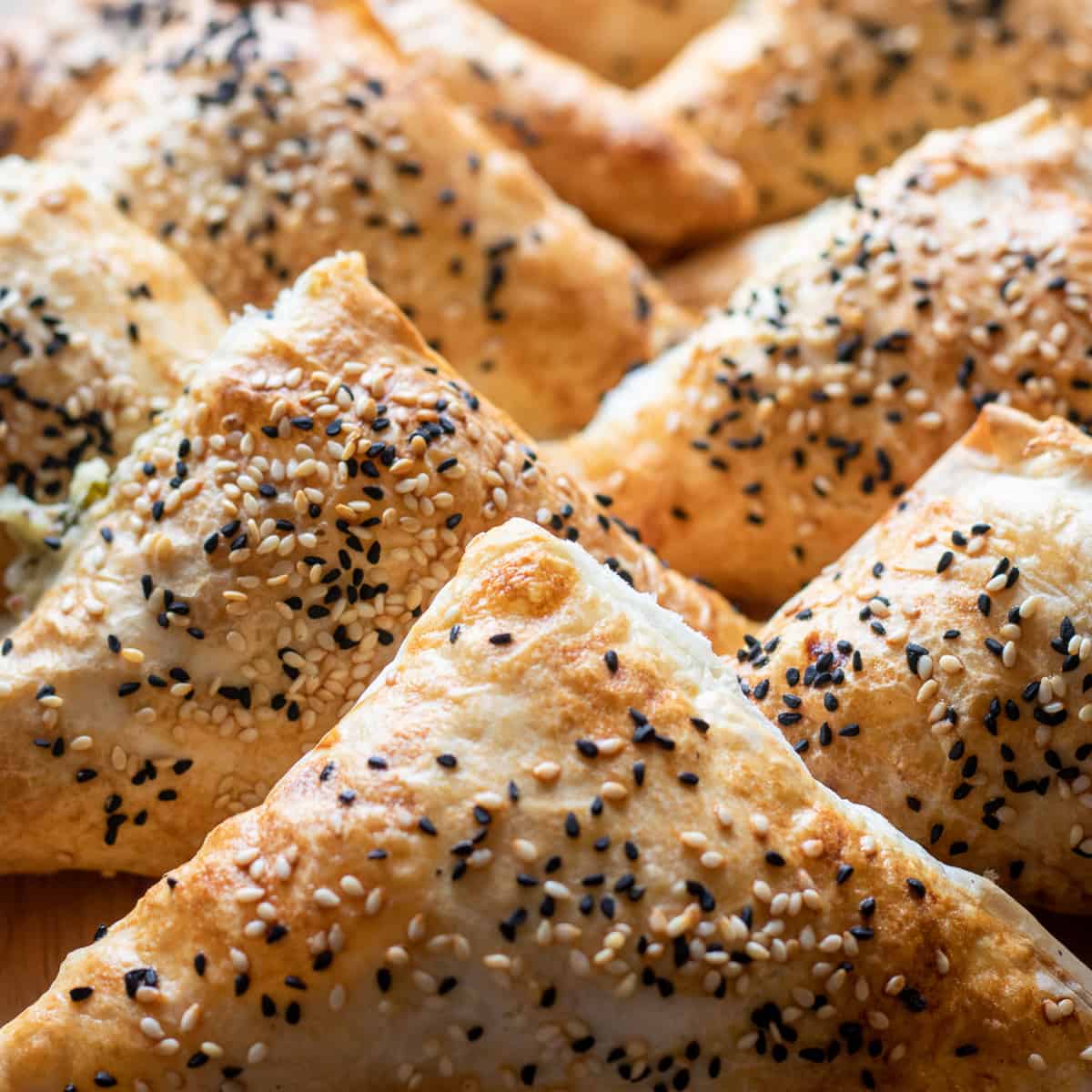 Overhead view of baked cheese borek triangles topped with sesame and nigella seeds on a baking tray.