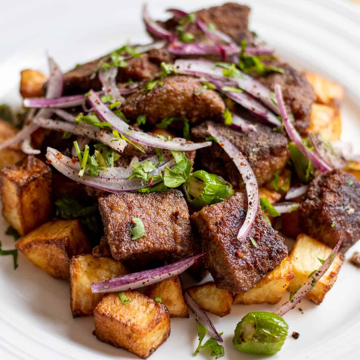 Arnavut Cigeri served on a white plate with crispy potatoes, sumac onions, and parsley.