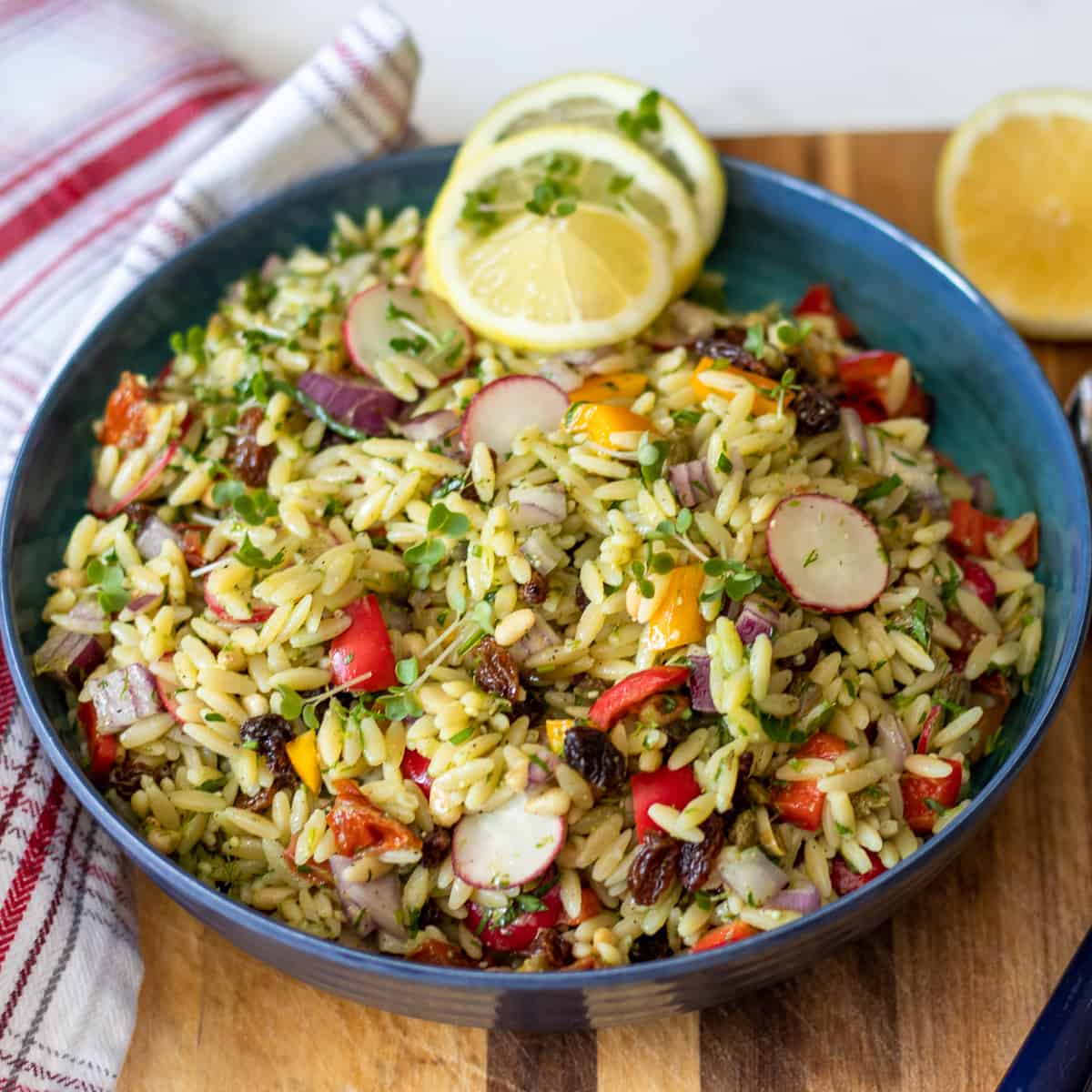 Overhead shot of orzo pasta salad with pesto in a blue bowl, garnished with lemon slices.