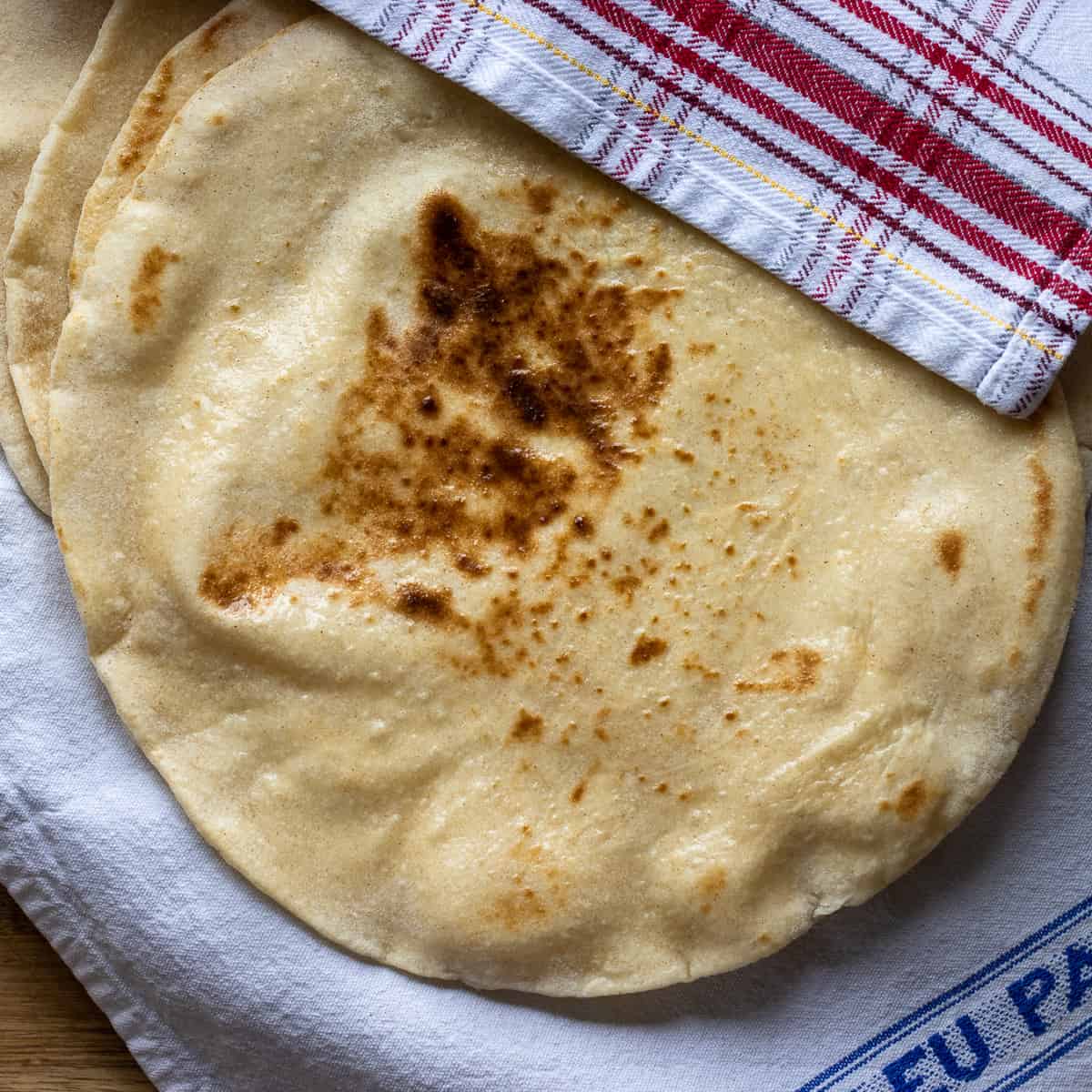 Stack of cooked sourdough flatbreads with charred spots on a kitchen towel.