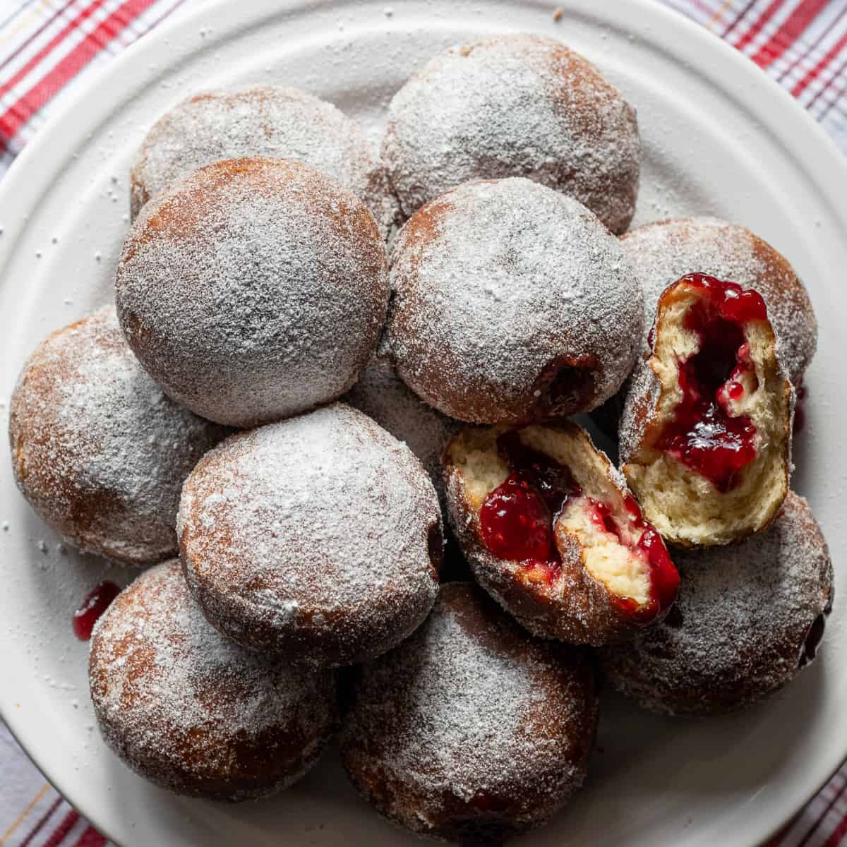 A plate of Berliner German jam donuts dusted with powdered sugar, one broken open to show the raspberry jam.