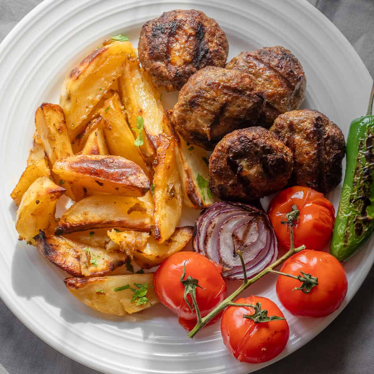 Grilled patties served with lemon roasted potatoes, tomatoes, and a charred green pepper.
